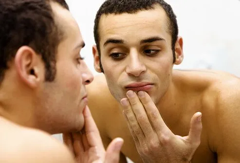 A man examines his skin in the mirror.