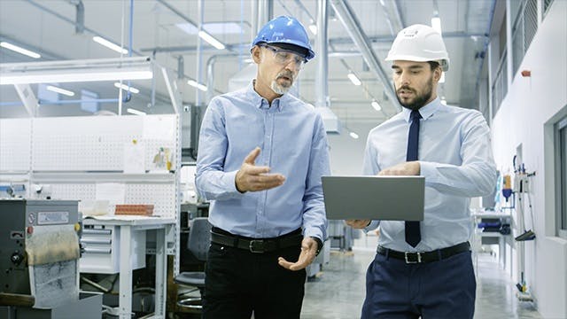 Two men talking and looking at a tablet. 