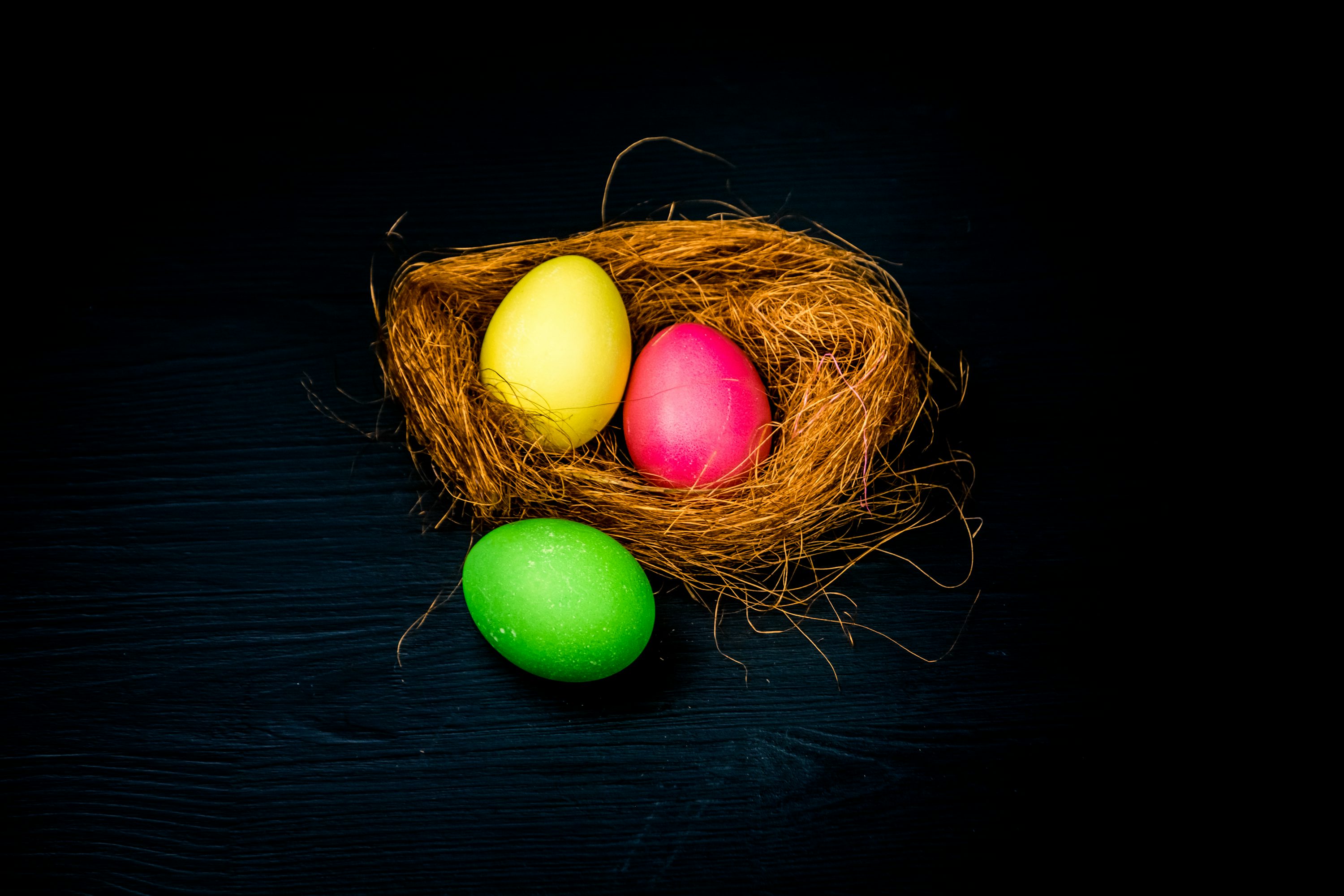 drei farbige Eier in einem Nest auf schwarzem Hintergrund