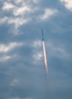 a jet flying through a cloudy blue sky