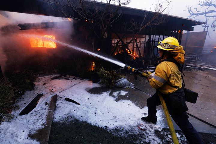 A firefighter tries to extinguish a fire as it damages a property in the Pacific Palisades neighborhood of Los Angeles Tuesday, Jan. 7, 2025. (AP Photo/Ethan Swope)