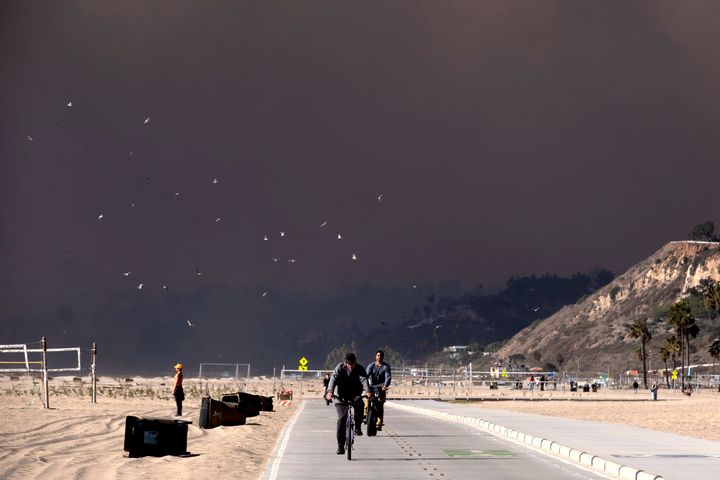 Bike riders make their way along the coast as large dark plume of smoke passes over the beach from a wildfire from Pacific Palisades, from Santa Monica, Calif. on Tuesday, Jan. 7, 2025. (AP Photo/Richard Vogel)