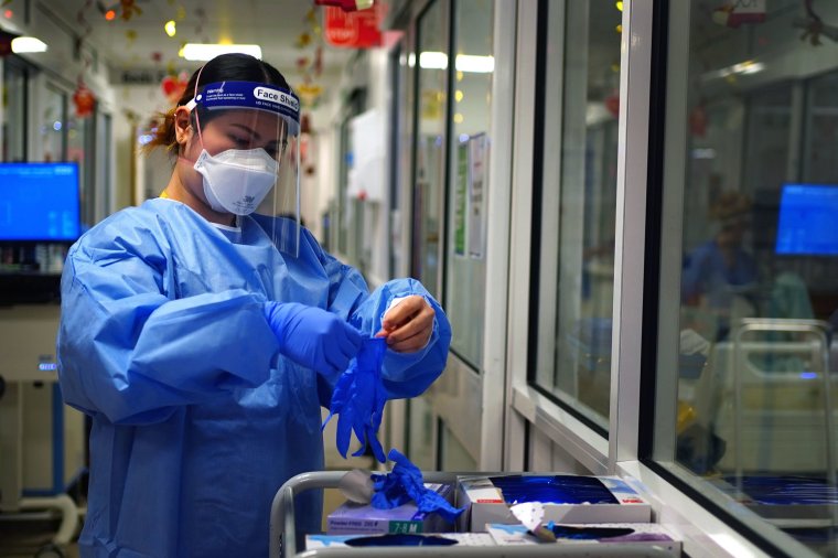 A nurse puts on PPE in a ward for Covid patients at King's College Hospital, in south east London. Picture date: Tuesday December 21, 2021. PA Photo. Medical staff at the hospital, where 102 coronavirus patients are in general beds and 18 are in critical care, have said they are holding out hope they will avoid a huge surge of admissions before Christmas as Omicron spreads across the capital, but are feeling the pressure over staff shortages due to Covid-related absences. See PA story HEALTH Hospitals. Photo credit should read: Victoria Jones/PA Wire