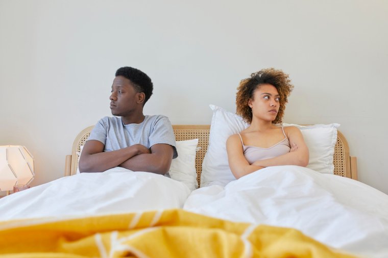 Young couple on bed, they are looking away from each other and look irritated.