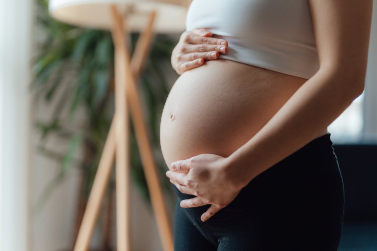 Side view close-up of pregnant woman touching her belly. Pregnancy health & wellbeing concept.