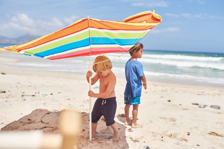 Shot of two little boys putting up an umbrella at the beach