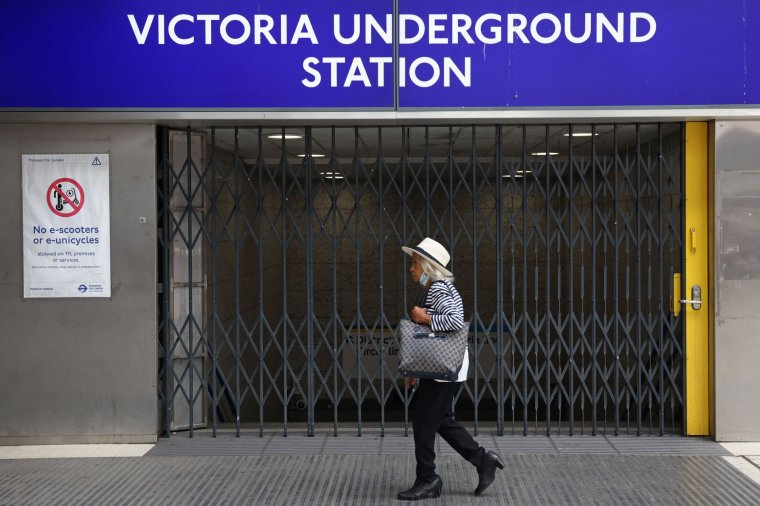 TOPSHOT - A pedestrian walks past the closed gates outside Victoria Underground Station London, on August 19, 2022, as strike action on Buses, National Rail and London Underground affects services. - Public transport workers in London held fresh strikes Friday over pay and conditions, cutting services on almost all underground and overground rail lines that link up the UK capital. (Photo by Hollie Adams / AFP) (Photo by HOLLIE ADAMS/AFP via Getty Images)