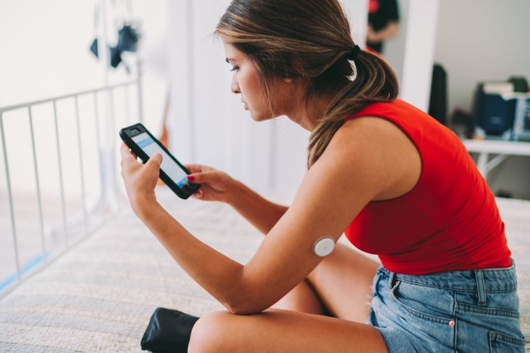 Young woman is wearing small sensor on the back of upper arm for measuring glucose levels due to diabetes. She checks whether the blood sugar is in normal range, after scanning the sensor with smartphone