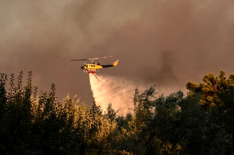 A helicopter drops a load of water over houses during a wildfire in Varnavas, north of Athens, on August 11, 2024. Greece was battling several wildfires on August 11, with smoke covering parts of the capital Athens in a haze, amid warnings for extreme weather conditions for the rest of the week. (Photo by Angelos TZORTZINIS / AFP) (Photo by ANGELOS TZORTZINIS/AFP via Getty Images)