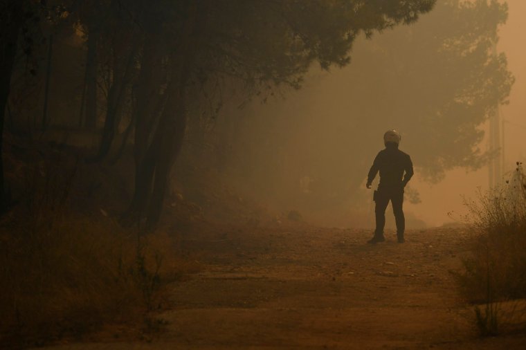 A police officer stands amidst smoke in Dioni, northeast of Athens, Greece, Monday, Aug. 12, 2024. Hundreds of firefighters backed by dozens of water-dropping planes and helicopters were battling the flames from first light Monday, with a major forest fire that began the previous day raging out of control on the fringes of Athens, fanned by strong winds. (AP Photo/Michael Varaklas)