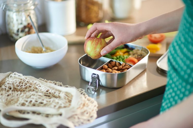 A woman at home packs an apple into her vegan plastic free lunchbox.