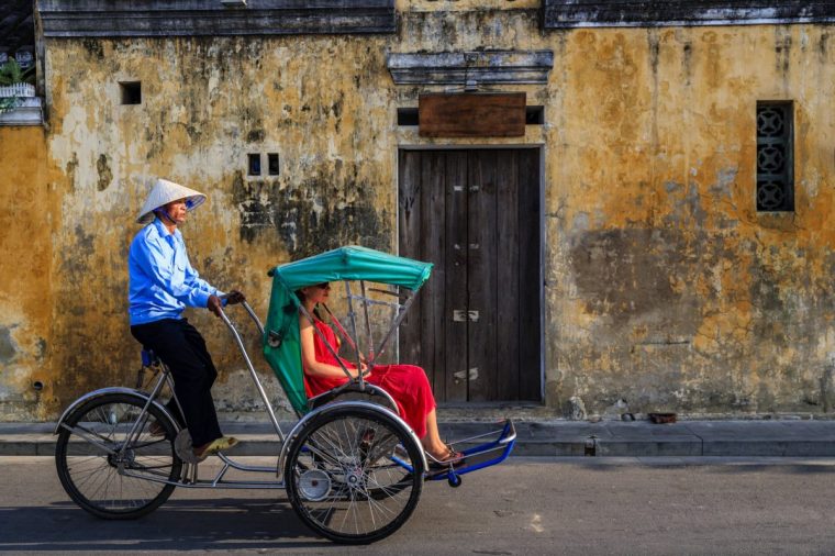 Vietnamese cycle rickshaw with caucasian young female tourist in old town in Hoi An city, Vietnam, old town in Hoi An city, Vietnam. Hoi An is situated on the east coast of Vietnam. Its old town is a UNESCO World Heritage Site because of its historical buildings.