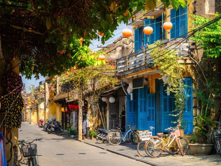 Picture shows one of the main street of Hoi An, Nguy???n Th??i H???c, empty during the day, in the heart of the old town, a UNESCO World Heritage Site since 1999. It is a picturesque pedestrian street lined with trees, colorful houses and lanterns. Picture shows several shops (gifts, bike rental) and restaurants.