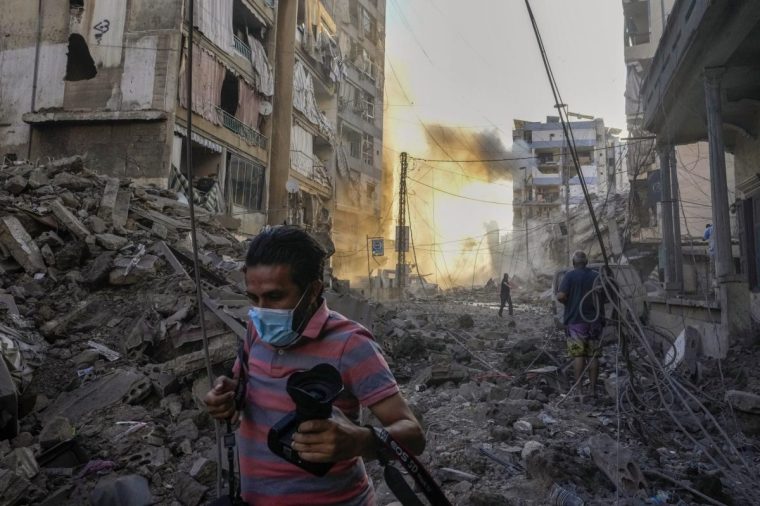 A photographer runs for cover as a smoke raises in the background following an Israeli airstrike in Dahiyeh, Beirut, Lebanon, Friday, Oct. 4, 2024. (AP Photo/Hassan Ammar)