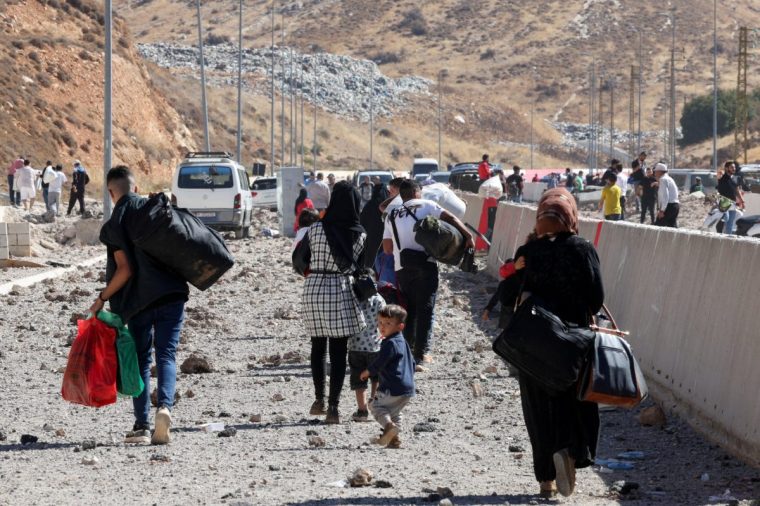 People carry their belongings while walking on the rubble, after an Israeli strike, as they flee Lebanon due to ongoing hostilities between Hezbollah and Israeli forces, at Masnaa border crossing with Syria, in Lebanon, October 4, 2024. REUTERS/Mohamed Azakir TPX IMAGES OF THE DAY