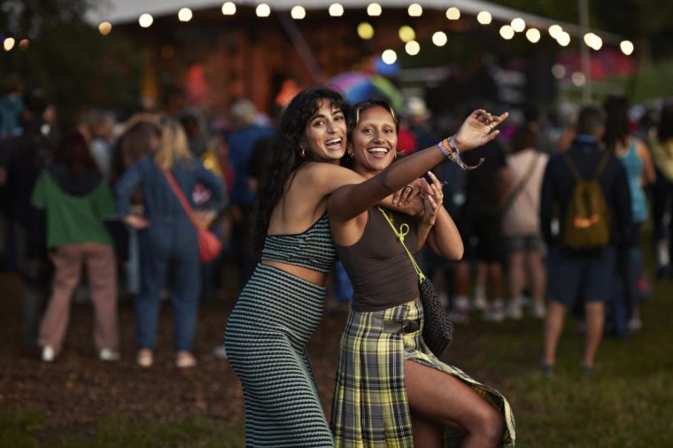 Portrait of cheerful woman hugging female friend from behind while enjoying at music concert