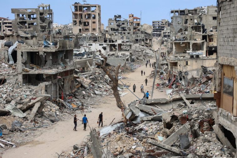 TOPSHOT - -- AFP PICTURES OF THE YEAR 2024 -- Palestinians walk on a dirt road lined with rubble from destroyed buildings in the Shujaiya neighbourhood of Gaza City on October 7, 2024, on the first anniversary of the ongoing war in the Gaza Strip between Israel and the Palestinian Hamas group. (Photo by Omar AL-QATTAA / AFP) / AFP PICTURES OF THE YEAR 2024 (Photo by OMAR AL-QATTAA/AFP via Getty Images)