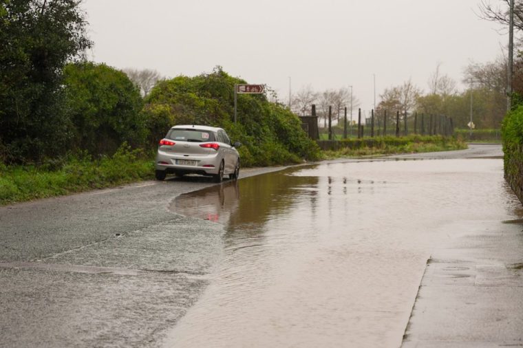 A car is driven past a flooded road at Passage West, Co Cork. Storm Bert is battering the country with strong winds, heavy rain and snow and ice with amber warnings coming into force bringing a "potential risk to life and property". Picture date: Saturday November 23, 2024. PA Photo. See PA story WEATHER Bert. Photo credit should read: Noel Sweeney/PA Wire