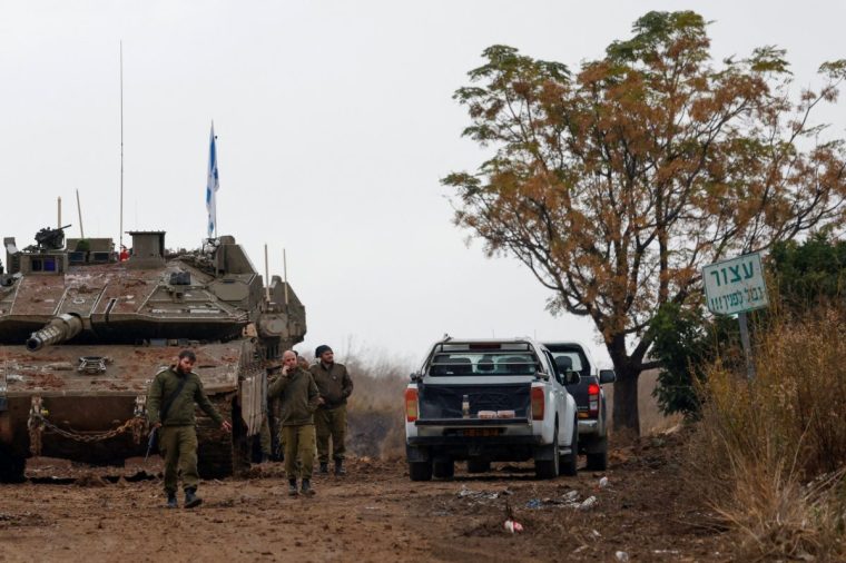 Israeli soldiers walk past a tank stationed near the border with Lebanon in the upper Galilee region of northern Israel during a change of shifts on November 27, 2024, after a ceasefire between Hezbollah and Israel took effect. A ceasefire between Israel and Hezbollah in Lebanon took hold on November 27 after more than a year of fighting that has killed thousands. (Photo by Jalaa MAREY / AFP) (Photo by JALAA MAREY/AFP via Getty Images)