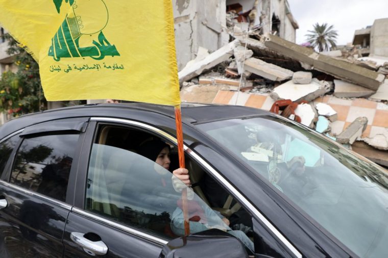 A resident waves a Hezbollah flag out of a car window in the southern Lebanese village of Zibqin on November 27, 2024, as people who had fled the war between Israel and Hezbollah returned to check on their homes after a ceasefire between the warring sides took effect. Under the terms of the deal that brought the war to a halt, the Lebanese military started reinforcing its presence in the country's south, where Hezbollah has long held sway. (Photo by Anwar AMRO / AFP) (Photo by ANWAR AMRO/AFP via Getty Images)