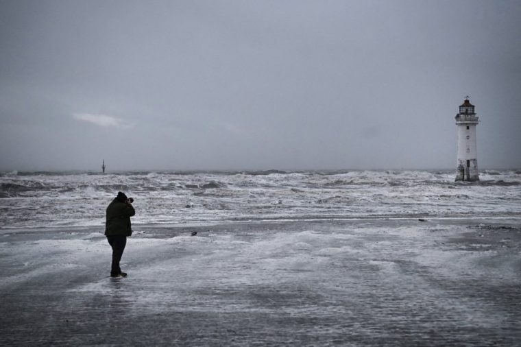 A man takes a pictures of New Brighton Lighthouse, also known as Perch Rock Lighthouse in the background, in New Brighton, near Liverpool, on December 7, 2024 as storm Darragh brings winds of nearly 90 mph to the west of Wales and north-west England. The UK's Met Office had issued a rare red alert for high winds overnight to Saturday morning (0300 to 1100 GMT) covering parts of Wales and southwest England. Tens of thousands of people across the UK were left without power on Saturday morning after Storm Darragh hit the country with strong winds and caused pre-Christmas travel disruption. (Photo by Paul ELLIS / AFP) (Photo by PAUL ELLIS/AFP via Getty Images)