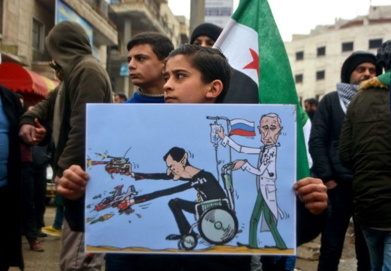 TOPSHOT - A young Syrian holds a caricature representing Syrian President Bashar al-Assad and Russian President Vladimir Putin as he takes part in a demonstration to protest against the continuing assault by the Syrian regime and Russian forces on the last rebel-held pockets in the northern Idlib province, in the city of Idlib on February 21, 2020. (Photo by Mohammed AL-RIFAI / AFP) (Photo by MOHAMMED AL-RIFAI/AFP via Getty Images)