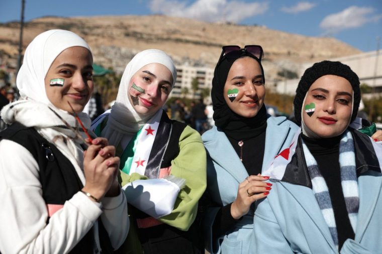 Young Syrian women with the independence-era flag, used by the opposition since the uprising began in 2011, painted on their faces pose for a picture during celebrations of this week's toppling of president Bashar al-Assad in Damascus' central Umayyad Square on December 13, 2024. Thousands of jubilant Syrians also gathered outside a landmark mosque in the capital Damascus to celebrate during the first Friday prayers since Assad's ouster on December 8. (Photo by OMAR HAJ KADOUR / AFP) (Photo by OMAR HAJ KADOUR/AFP via Getty Images)