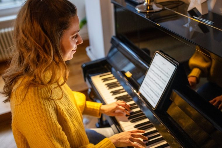 Beautiful woman playing piano at home. Caucasian female learning playing the piano with notes on a tablet computer.