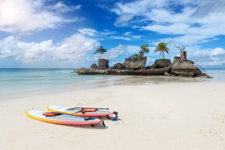 Surfboards on the White Beach, in the background the iconic rock with Mother Mary (Willy s Rock). White Beach on Boracay island has been voted one of the most beautiful beaches in the world.