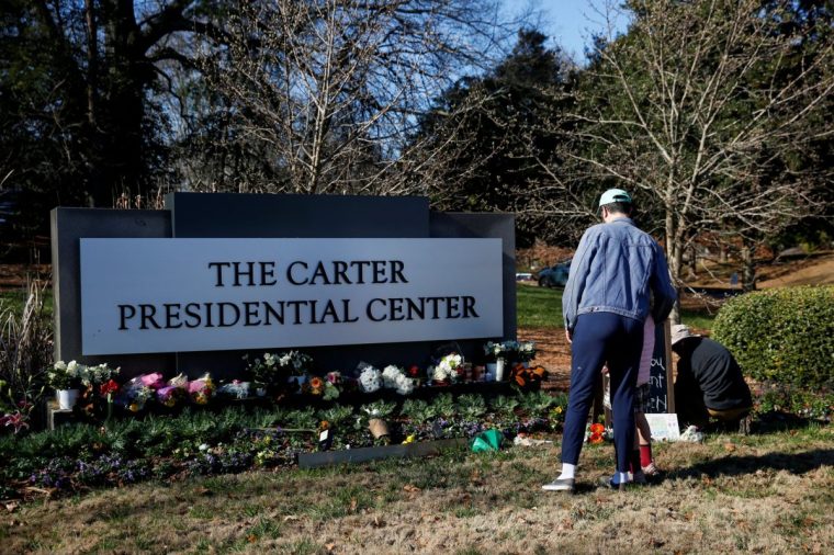 Nick Lynton stands with his daughter, as he pays his respects to former U.S. President Jimmy Carter, who died at the age of 100, by the sign of The Carter Presidential Center, in Atlanta, Georgia, U.S. December 30, 2024. REUTERS/Octavio Jones