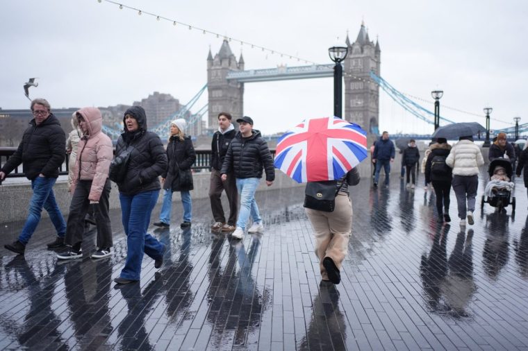 People during a rain shower at More London on the south bank of the River Thames near Tower Bridge, London, as a new yellow weather warning for rain has been issued for southern England on Sunday. Elsewhere, heavy overnight snow is causing disruption across parts of the UK as the cold start to the new year continues. Picture date: Sunday January 5, 2025. PA Photo. Two amber weather warnings from the Met Office have been put in place in England and Wales, with 3cm to 7cm of snowfall predicted for much of the affected area, mixing with rain at times in lower-lying areas. The Met Office said Bingley, West Yorkshire, had seen 12cm of snow up to 7am on Sunday, with Shap in Cumbria and Capel Curig, Gwynedd, both seeing 10cm. One amber warning for snow and freezing rain, which covers much of Wales and the Midlands as far north as Manchester, is in place until midday on Sunday. See PA story WEATHER Winter. Photo credit should read: Yui Mok/PA Wire