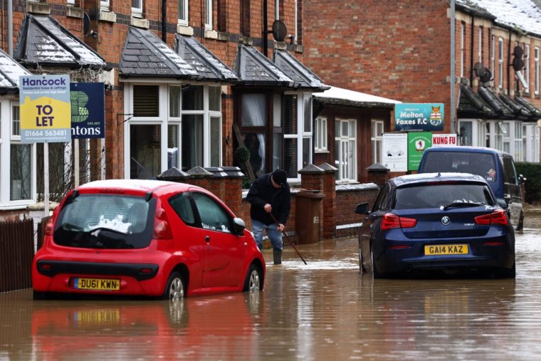 People wade through flood water outside houses in Melton Mowbray, central England, on January 6, 2025, following torrential rain that caused localised flooding. (Photo by Darren Staples / AFP) (Photo by DARREN STAPLES/AFP via Getty Images)