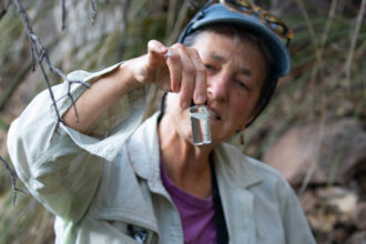 Kerry Schwartz, a retired hydrogeology faculty member and water resources educator at the University of Arizona, holds up a small sample of water from the spring in Alum Gulch. Credit: Esther Frances/Inside Climate News