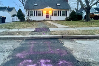 A house with its lights on is in the background. In the foreground: "GEO" spray painted in purple on the sidewalk leading up to it.