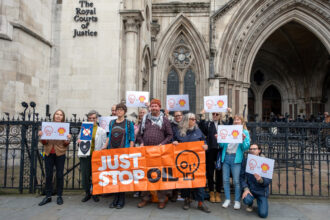 Emma Ireland and Charles Philip Laurie from Just Stop Oil pose with their supporters outside of the Royal Courts of Justice in London before their hearing on Oct. 22. Credit: Keerti Gopal/Inside Climate News