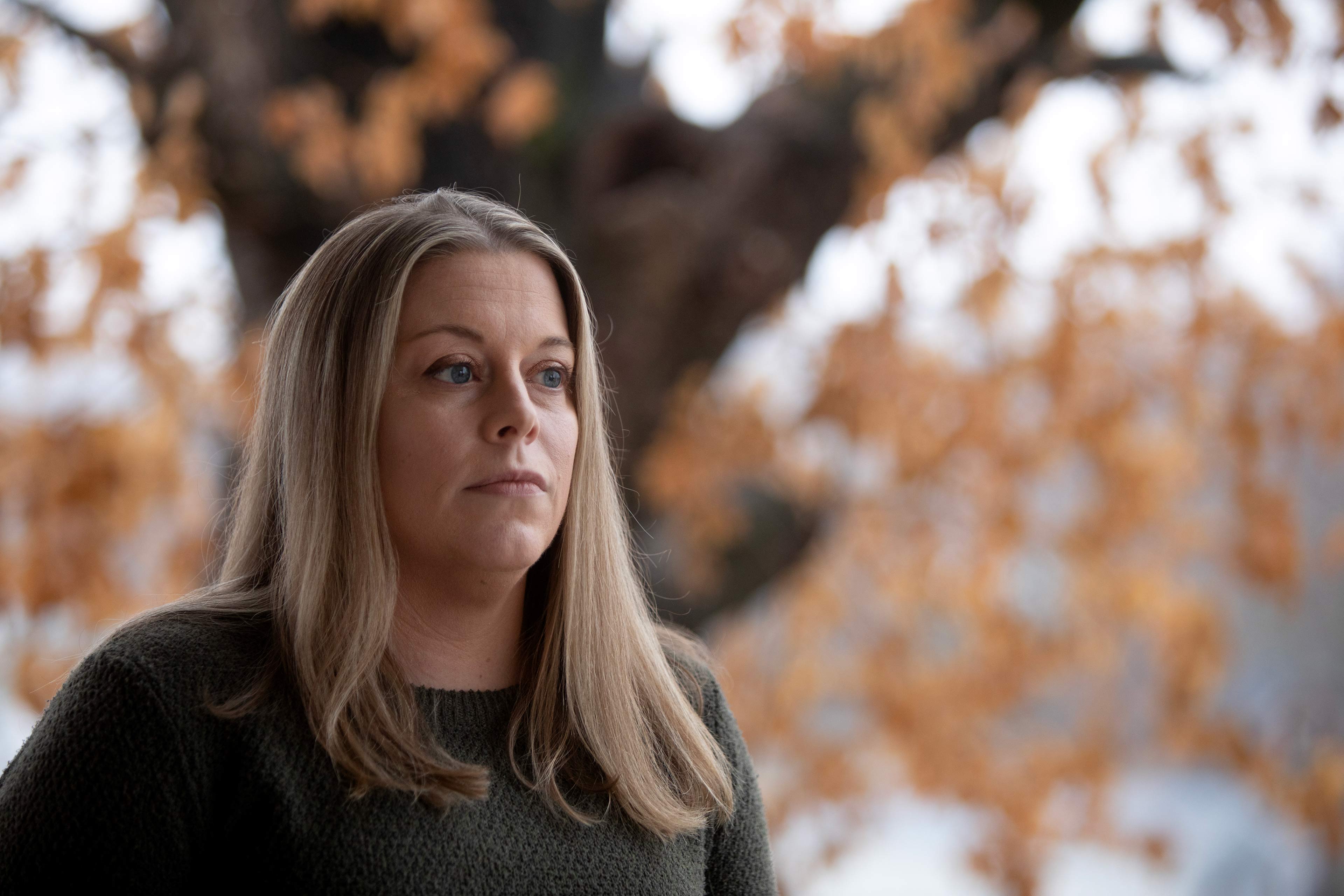 A photo of a woman standing outside in front of a tree.