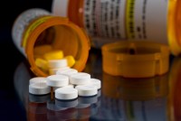 An up-close photo of a tipped-over prescription bottle against a black background. Opioid painkiller pills spill out of the bottle.