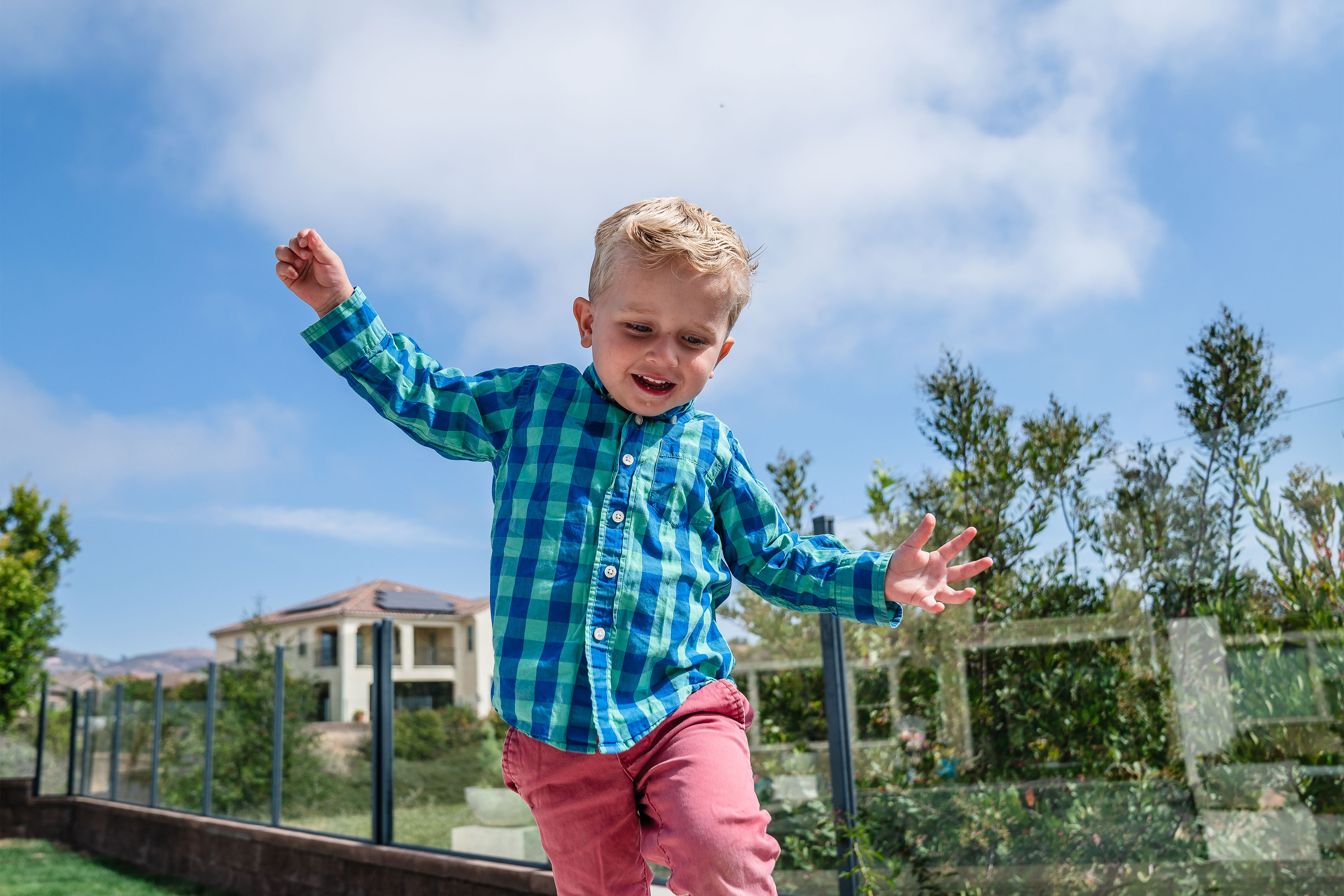 A young boy runs outside with both arms outstretched.