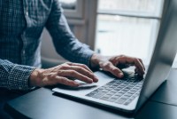 A cropped shot of a man typing on the keyboard of a laptop at home.