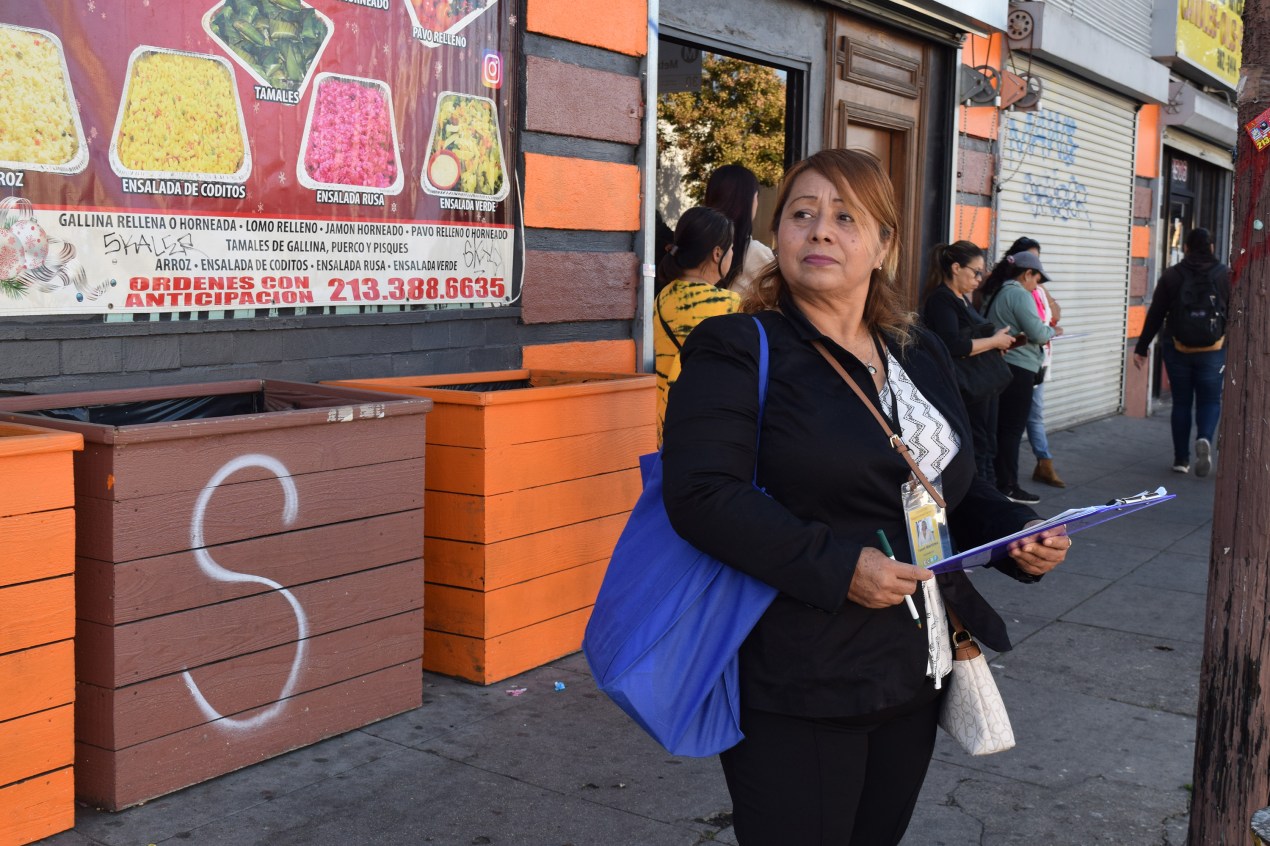 A photo of a Latina woman standing outside with a clipboard.