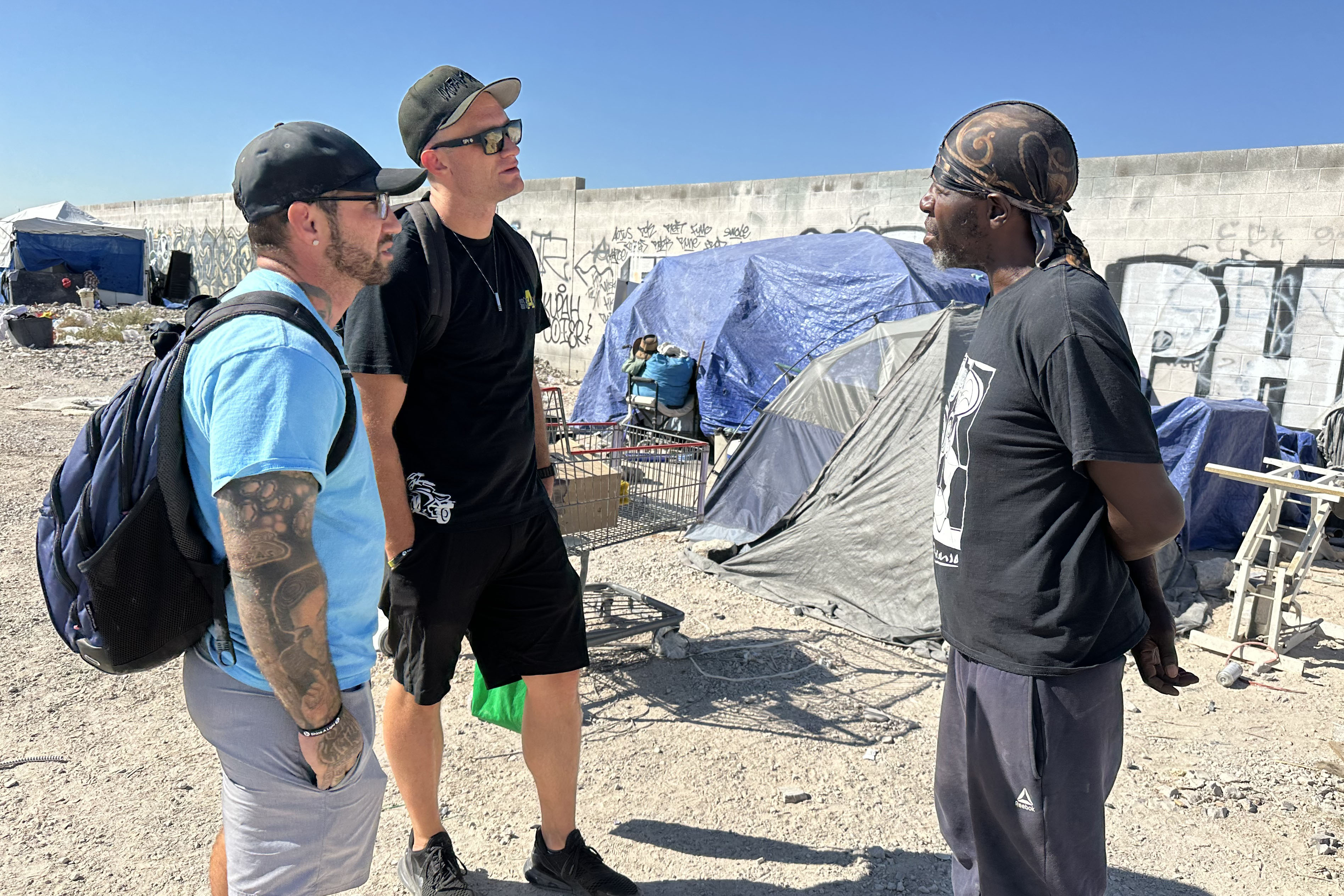 Outreach workers Bryon Johnson (center) and Nick Freddes (left) talk to Maurice Clark, a Black man who is homeless.