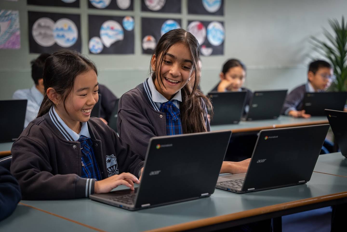 Two smiling students work together on a laptop in a classroom.