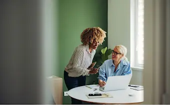 Deux femmes sont réunies devant un ordinateur portable pour travailler.