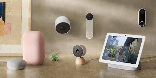 An array of Nest devices, including doorbells, speakers, displays, cameras and more are all laid out on a table and installed on a wall.