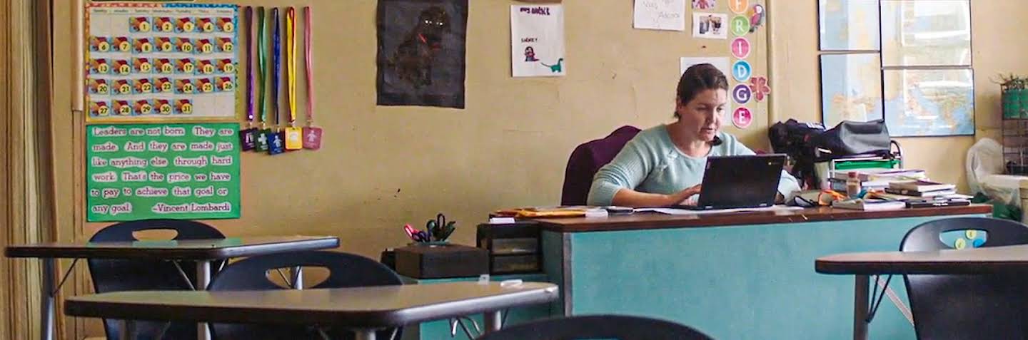 A student wearing a mask sits at their desk and engages with a laptop.