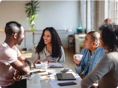 Cuatro personas de diferentes géneros y rasgos étnicos conversan mientras beben café.