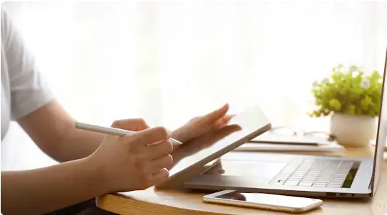 Un propriétaire d’entreprise est assis chez lui et travaille sur une tablette. Un ordinateur portable et un téléphone intelligent sont également posés sur la table, devant lui.