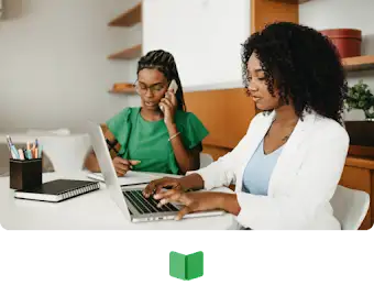 Una mujer trabajando al teléfono mientras toma notas y otra trabajando con su portátil.