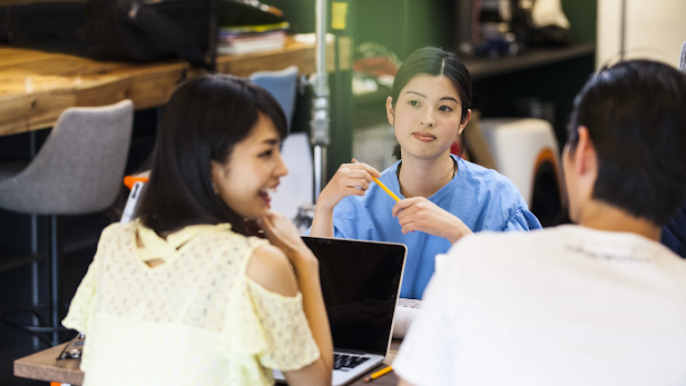 Asian women Googlers with laptops and pencils in front of them, engaging in conversation