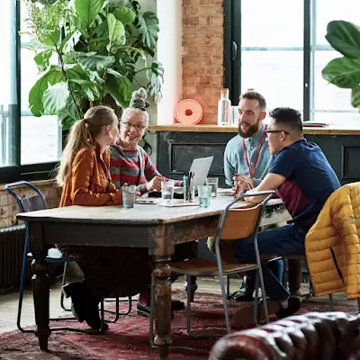 4 collega’s rond een vergadertafel in een kantoor dat wordt omgeven door planten.